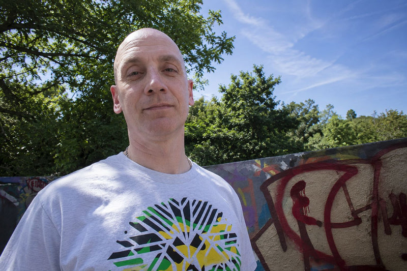 Gav Pauze wearing a Pauzewear graphic tee, standing in front of a graffiti wall outdoors