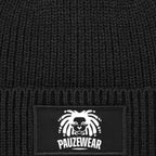 Black knit beanie with a white logo patch on a textured black background